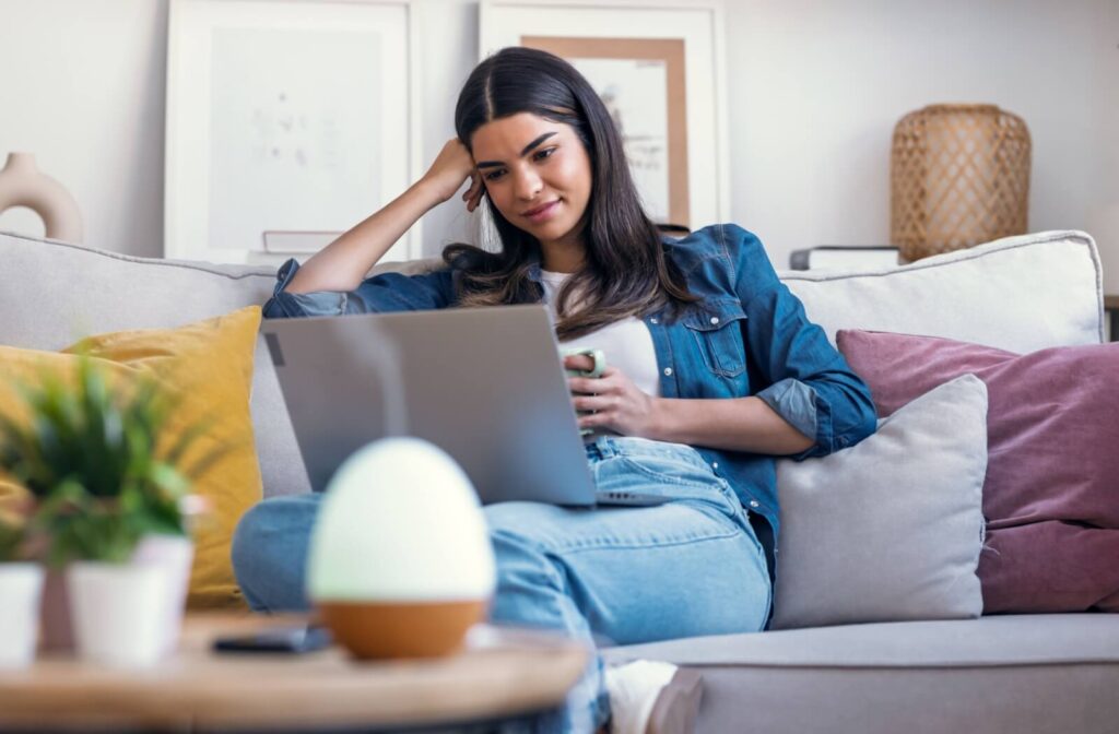 Person using a laptop at home with a humidifier nearby, illustrating common causes of dry eyes such as screen time, indoor air, and prolonged digital device use.