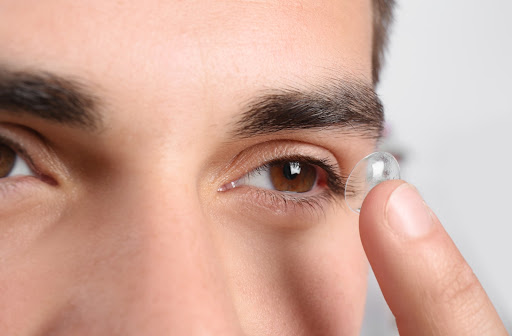 A close up image of a man putting a contact in his left eye.