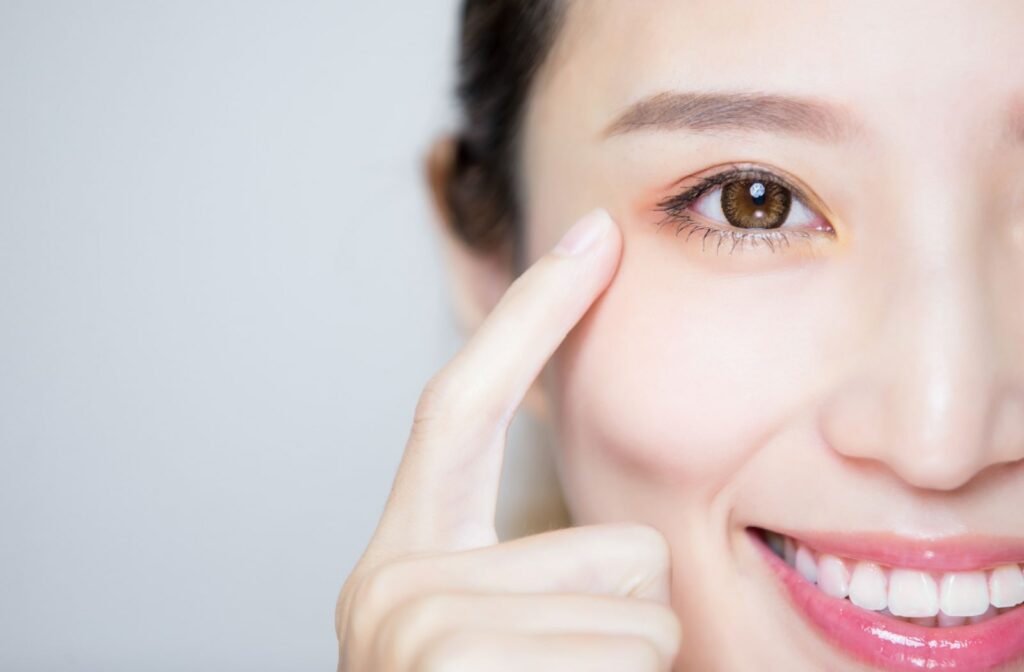 A close-up of a young woman with her right index finger pointing to her healthy right eye
