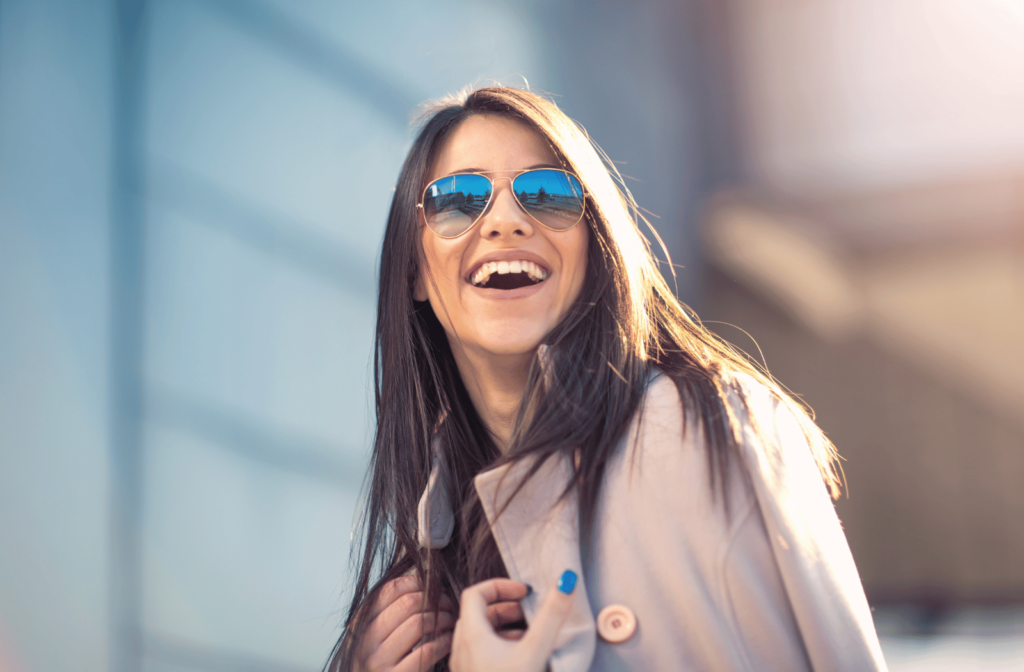 A young woman wearing a jacket and polarized sunglasses laughing