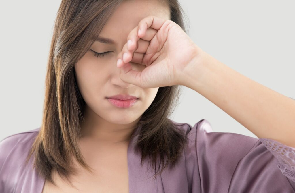A young woman waking up and rubbing her eyes due to dry eye issues in the morning