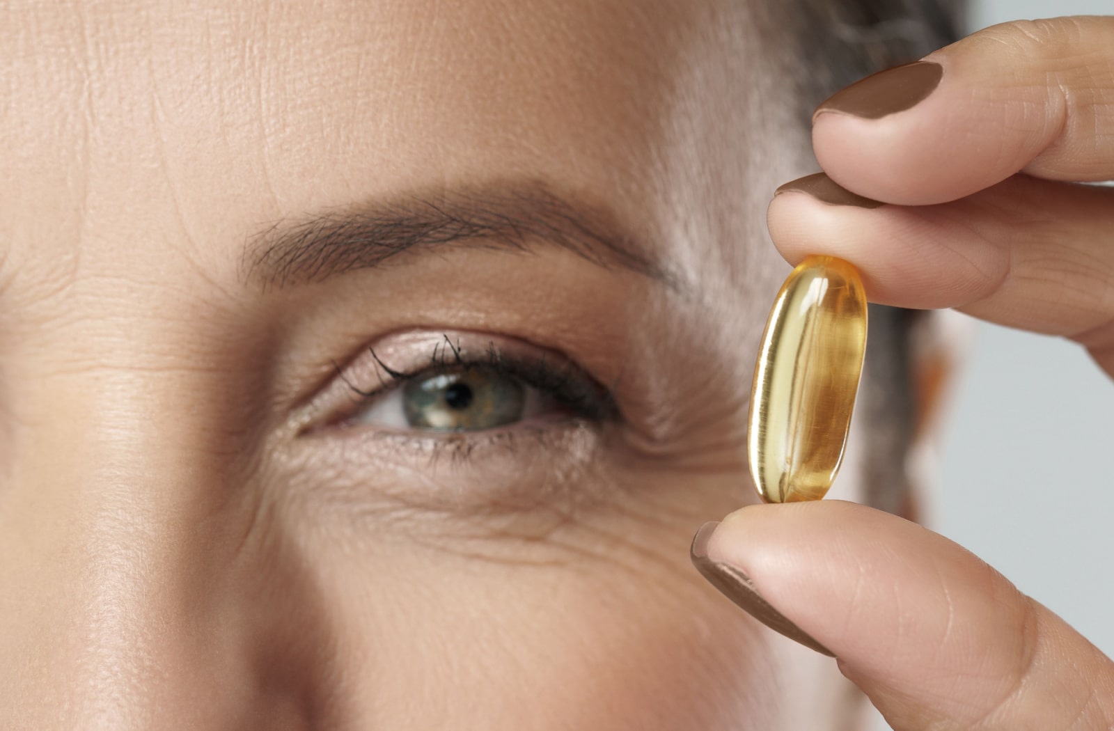 A woman holds up an Omega 3 vitamin next to her eye