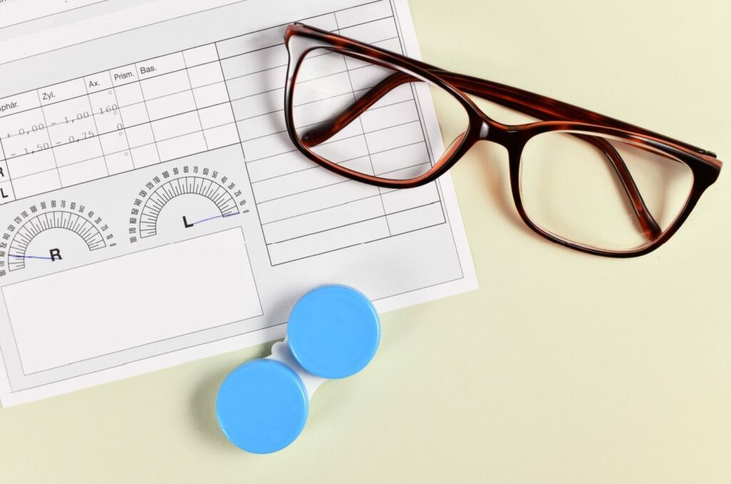 Eyeglasses & a contact lens case sit on top of a paper prescription.