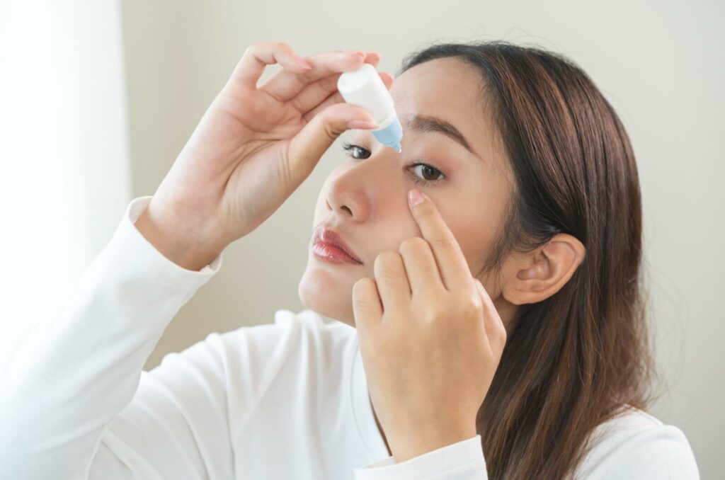 A young woman applying eye drops to her dry eyes.