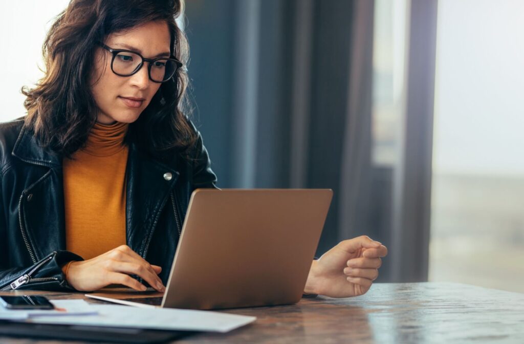 A person wearing glasses working on a laptop, representing the link between digital eye strain, chronic dry eyes, and frequent headaches.